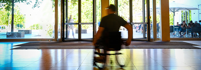 Rollstuhlfahrer fährt rasch durch ein Universitätsgebäude